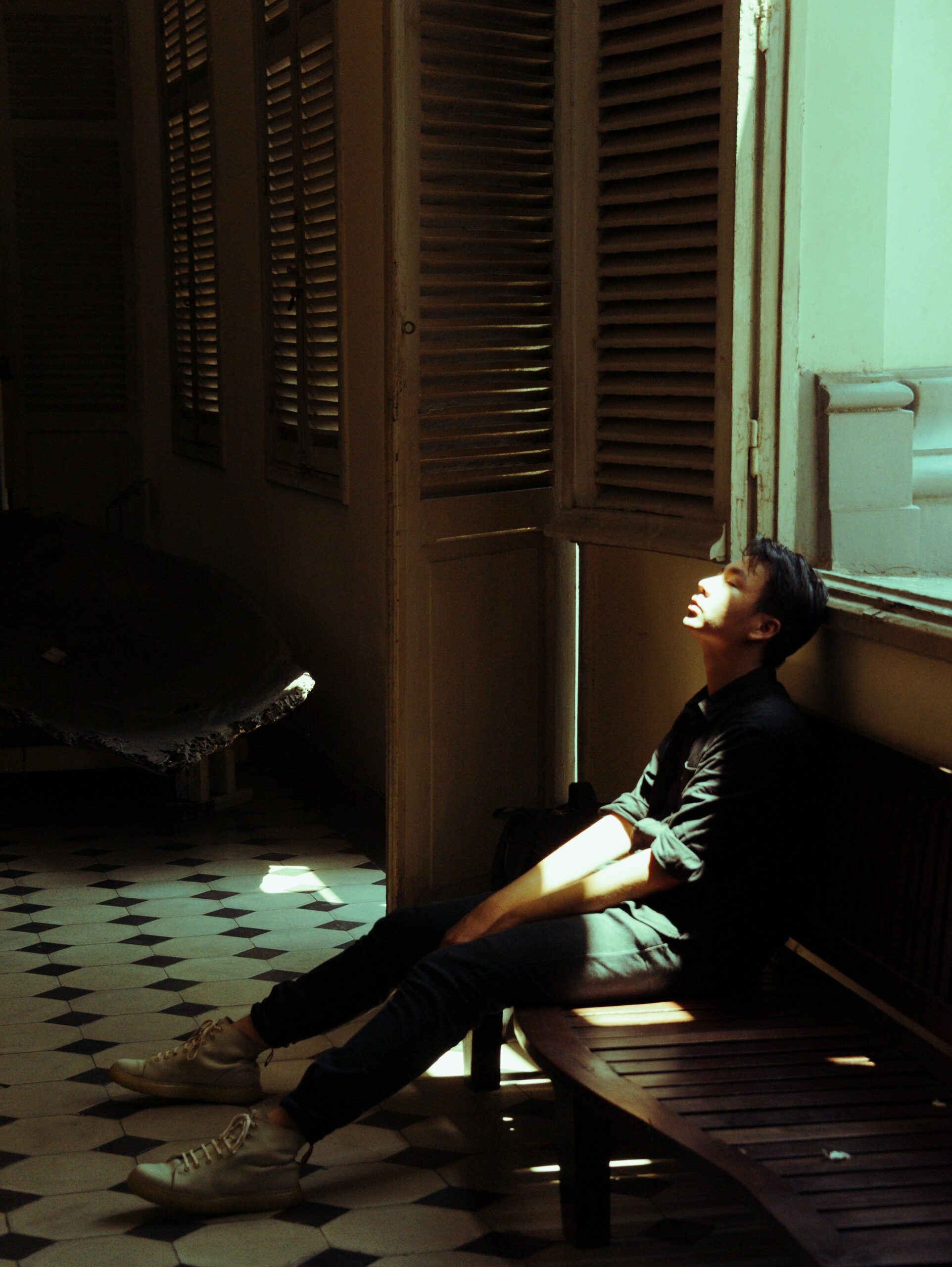 A young man sits in a dimly lit room, soaked in sunlight, depicting introspection.